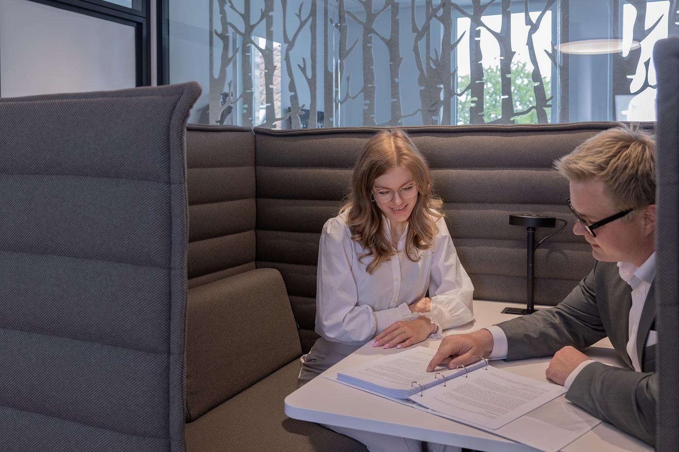 Zwei Personen sitzen an einem Tisch und schauen sich Dokumente an.